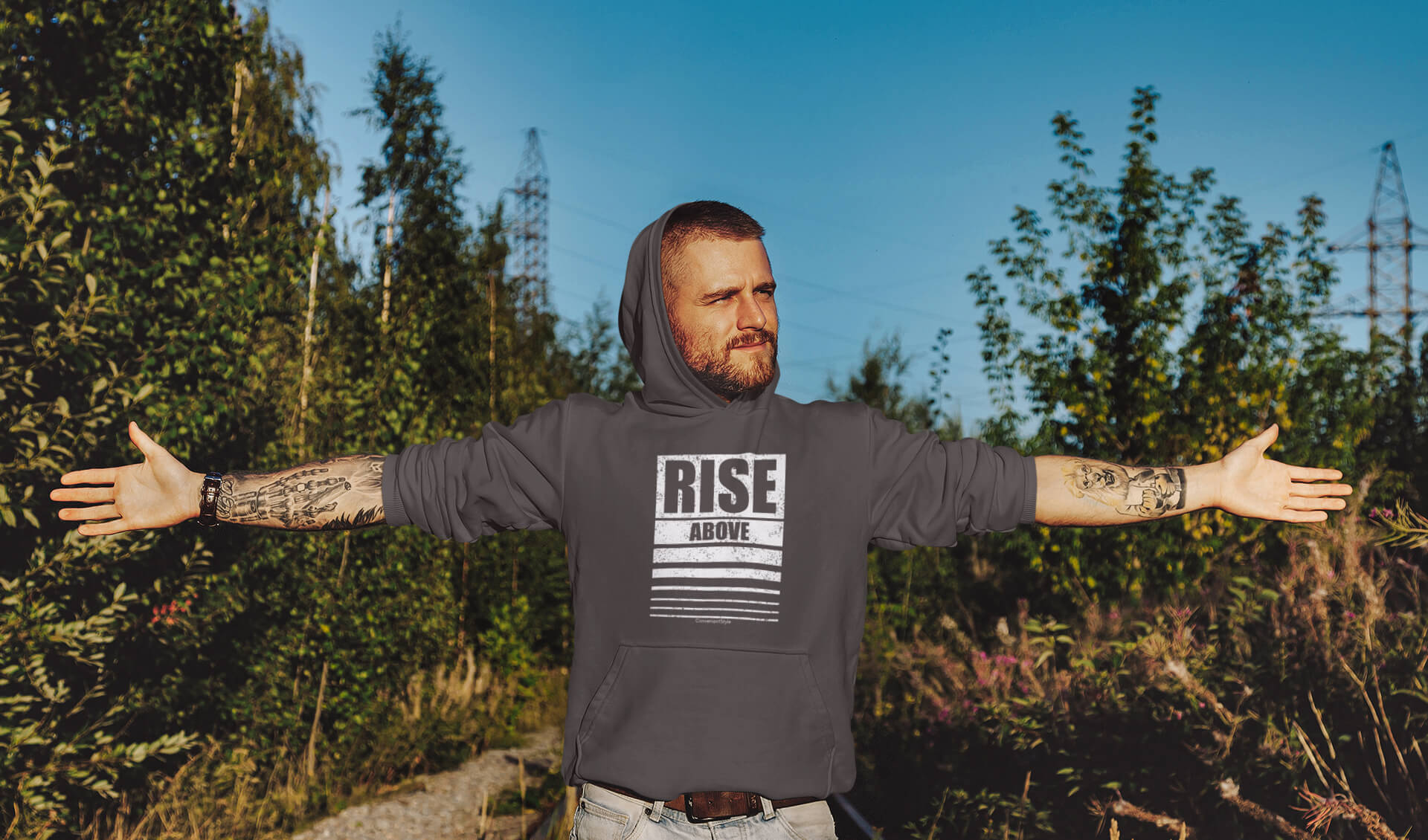 Tätowierter Mann mit ausgestreckten Armen und 'Rise Above' T-Shirt symbolisiert Achtsamkeit, Ziele erreichen, Resilienz und persönliches Wachstum